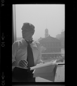 Mayor White standing by a window in his City Hall office overlooking Faneuil Hall and reviewing papers