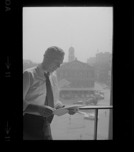 Mayor White standing by a window in his City Hall office overlooking Faneuil Hall and reviewing papers