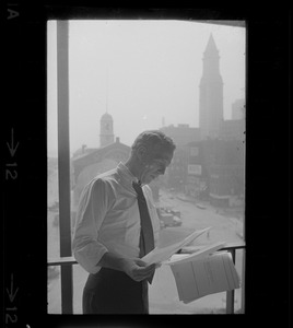 Mayor White standing by a window in his City Hall office overlooking Faneuil Hall and reviewing papers