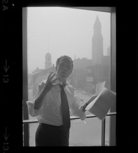 Mayor White standing by a window in his City Hall office overlooking Faneuil Hall and reviewing papers