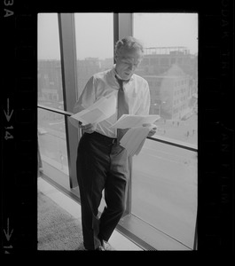 Mayor White standing by a window in his City Hall office overlooking Faneuil Hall and reviewing papers
