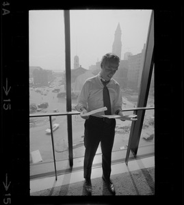 Mayor White standing by a window in his City Hall office overlooking Faneuil Hall and reviewing papers