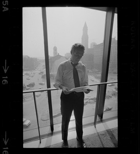 Mayor White standing by a window in his City Hall office overlooking Faneuil Hall and reviewing papers