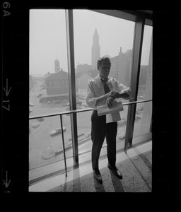 Mayor White standing by a window in his City Hall office overlooking Faneuil Hall and reviewing papers