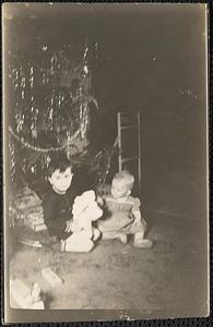 Two toddlers seated under a Christmas tree