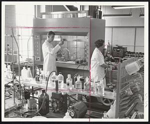 In New England Nuclear Corp. laboratories such as this one, chemicals are synthesized to achieve the exotic radioactive chemicals necessary for many phases of scientific research. Here, Charles Hainley, a chemist, examines the composition of one of the chemicals. The corporation has more than 400 compounds in stock, the largest supply of radioactive chemicals in the country.