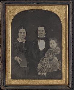 A seated woman holding a book next to a seated man holding a girl