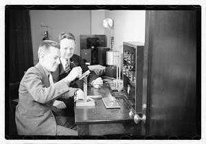 A boy sitting next to a man using an unidentified device