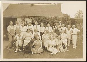 Group of men and women posed in front of a garage or house