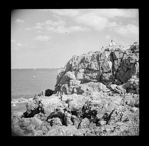 People on rock outcropping, sailboats in distance