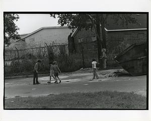 Children playing in a courtyard, one bouncing on a mattress