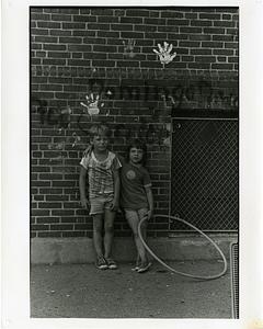 A boy and a girl with a hula hoop leaning against a brick wall