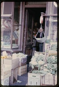 A scale hanging in front of a store selling vegetables