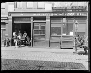A horse drawn cart exiting the storefront of Havilah M. Smith & Son, Carpenters