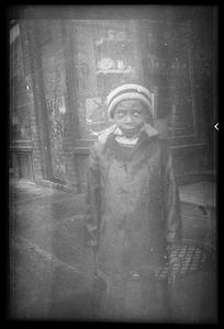 A boy wearing a hat stands in front of a storefront and manhole cover