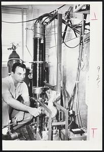 Technician Lew Burkhardt adjusts valve (left) alongside coil-wrapped upright tube which is heart of hydrogen fusion experimental device at Atomic Energy Commission's Los Alamos, N. M., laboratory. Tube encases smaller container of heavy hydrogen gas.