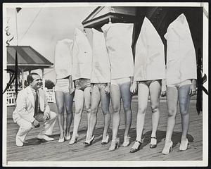 Selecting the Most Beautiful Legs. These girls are neither ghosts nor members of the Ku Klux Klan, but entrants in the contest to select the girl with the most beautiful legs. Flour sacks were placed over the girls' heads to prevent the judges and Mr. Louis Zinberg (left), who presented the awards, from being swayed in their selections by pretty faces and figures. Miss Cecille Joseph of New York City (extreme right) was the winner.