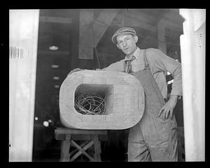 A man posing with an unidentified wooden item with wires in the middle