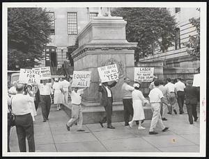 State Workers march around statue of General Hooker outside the State House today. They are seeking pay raises for all state employes. Meanwhile, a hearing on pay raises for University of Massachusetts faculty was under way in the State House.