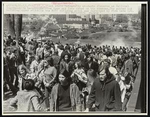 Kent State University students disperse as National Guardsmen(in background)fire tear gas into crowd on the commons. The gutted out building(upper right)is the ROTC building which was destroyed by fire late 5/2.