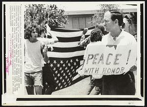 Both Sides of the Street--As peace demonstrators carry an American flag upside down in their parade near President Nixon's Key Biscayne home today Thomas K. Meakin walks on the other side of the street with a sign asking for peace with honor. Meakin lives a few doors away from Nixon's home.