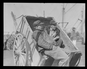 Two men rest in hand cart at fish pier