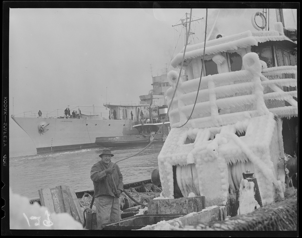 Ice covered fishing trawler with ship "Charleston" in background