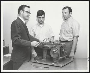 Do Nothing Machine,' that screens, selects and trains mechanics by simulation device has been developed by Anderson-Nichols & Co., Inc. Here, Richard J. Whouley, project director explains the Standard Timing Model to a couple of machine adjuster candidates. Many major U. S. firms use device.