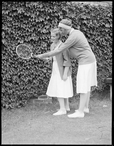 Polly Morrill is shown how to hold a racquet by her sister, Mrs. Whitfield painter, formerly Marjorie Morrill, at Longwood