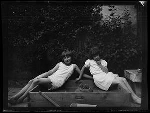 Two young girls posing seated in sandbox