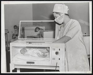 New Use for Incubators is demonstrated by this normal baby boy who is spending his first day of life in an incubator at Massachusetts Memorial Hospitals. Student Nurse Alice Jones of Nantucket is about to wake him up for feeding. Baby is five pounds, 15 ounces.