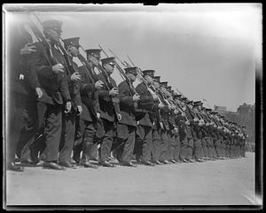 A line of men in military uniform marching, all holding rifles