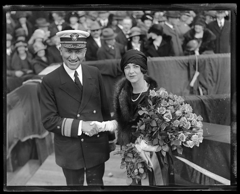 Unidentified woman holding a bouquet of flowers shaking hands with an admiral