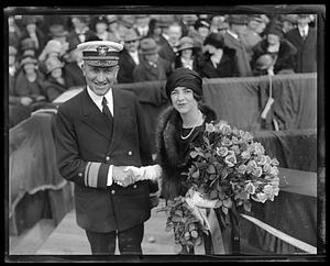 Unidentified woman holding a bouquet of flowers shaking hands with an admiral