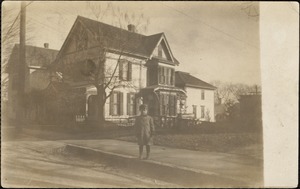 Young boy wearing a coat, standing on sidewalk, with a house in the background