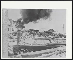 Oil Smoke Forms the Backdrop -- While a photographer looks at the wreckage, smoke rises in the background from burning oil storage tanks at Valdez. City was hard hit by the earthquake which demolished some of Alaska's most picturesque and largest cities.
