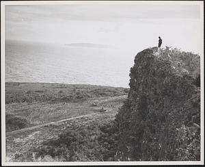 On Tinian island Marines look down upon their tanks and comrades from their cliff position