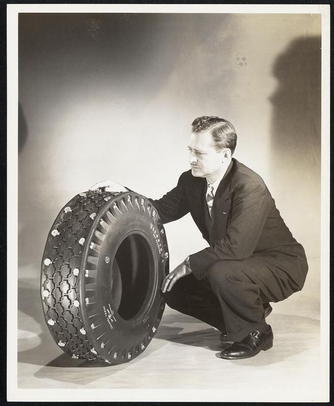 Removable steel lugs, used in tire manufacture for the first time, keep this airplane tire from skidding on ice, and permit all-weather use of the tire on combat planes. Examining the lugs and the bolts which hold them in place is Wilbur Shaw, three-time winner of the 500-mile Memorial Day automobile race and Sales Manager of the Firestone Aircraft Company, which developed the new ice tire.