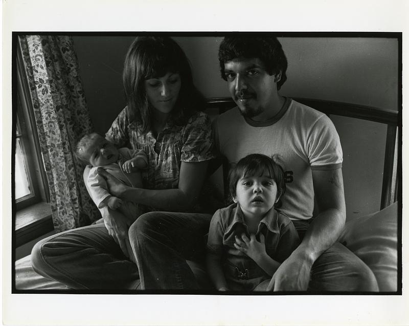 Portrait of a woman, a man, and two children sitting on a bed