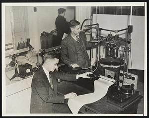 Measure Temperature Within Millionth of a Degree. Using an instrument that will measure temperature changes down to a millionth of a degree, a group of Northwestern University chemists are studying basic problems connected with amino acids which are closely related to hemoglobin in the blood and other protein substances which are still a mystery to scientists. Intended for use in the study of infinitesmal heat changes, the instrument, called a micro-calimeter by its inventors, Prof. Frank T. Gucker, Dr. Hugh Pickard and Dr. Ralph Planck of the chemistry department, can measure the amount of heat produced when sugar dissolves in water. Amino acids are formed by the decomposition of proteins in water, and the temperature changes are recorded on a scale so enlarged that one degree would qual a mile if the measuring rod were extended that long. Photo shows Dr. Pickard at the recording chart, foreground, as Prof. Gucker studied the sealed vessels in which solutions are placed during experiments. Changes in temperatures in one sealed vessel are determined by measuring the amount of electrical energy required to heat the water in another vessel to the same degree.