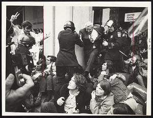 A man, being helped by police, stepping over seated protesters at Boston City Hall Plaza