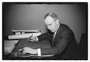 A man seated at a desk, blueprints in front of him