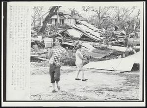 The Loss Was Almost Total-- Gary McGinn of Biloxi, Miss., carries a few pots he saved from the ruins of a fish factory where he worked until Hurricane Camille hit here Monday. His wife and child survey damage. McGinn said these were the only things he found worth keeping from the wreckage.