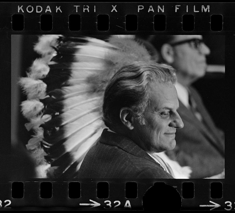 Billy Graham juxtaposed with Indian head dress, Plymouth