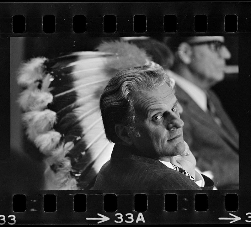 Billy Graham juxtaposed with Indian head dress, Plymouth