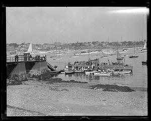 A group of people and boats gathered around a larger ship