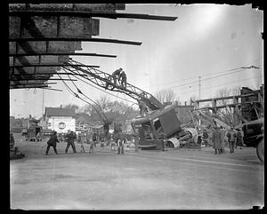 Workers managing a crane which is leaning to one side by some debris
