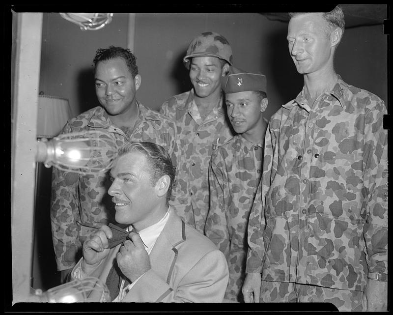 A man ties a bow around his neck while four men in "Jungleers" uniform watch