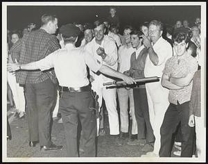 A group of men smile, a man holding a billy club in foreground