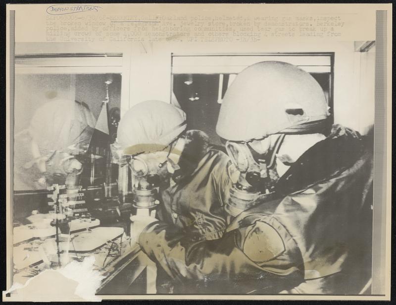 Berkeley, Calif: Oakland police, helmeted, & wearing gas masks, inspect the broken window of a Telegraph Ave. jewelry store, broken by demonstrators. Berkeley police, aided by officers from neighboring communities, used tear gas to break up a milling crowd of some 4,000 demonstrators and others blocking 4 streets leading from the University of California late 6/29.